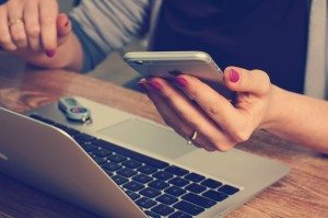 a woman using her smartphone while also using the computer