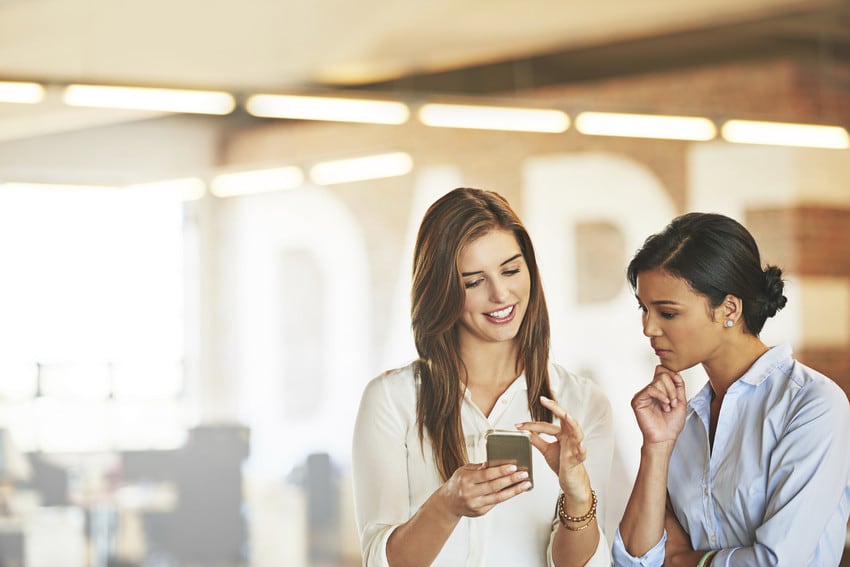 Two women looking at a cell phone and syncing their apps.