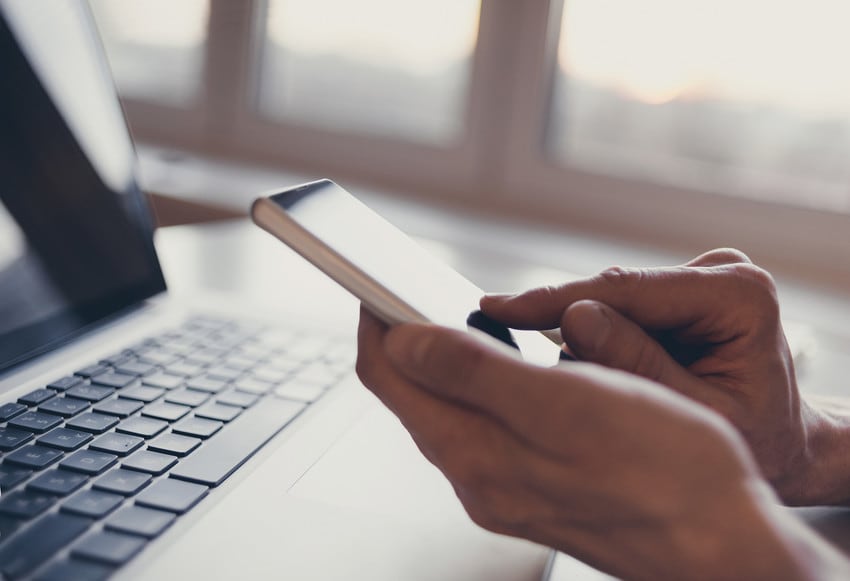 A person holding their smart phone in front of their computer.