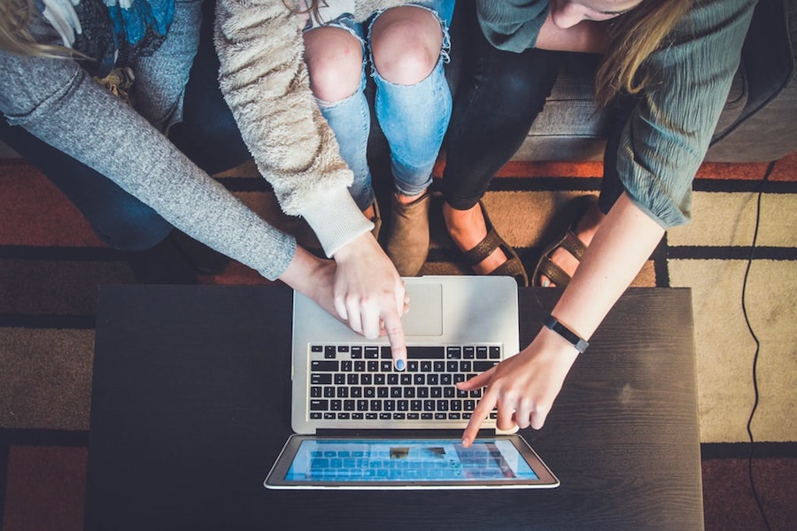 People pointing at social media logins on a laptop screen.